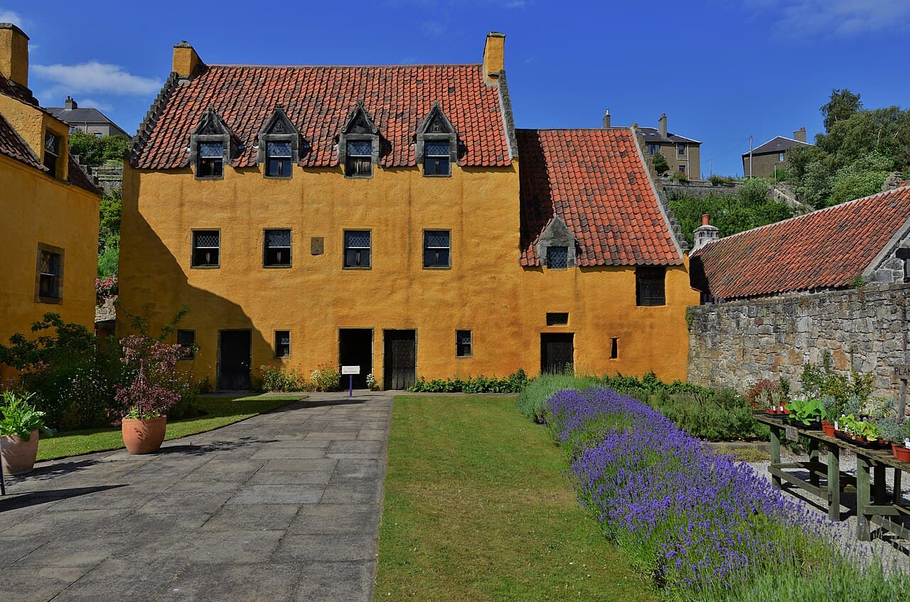 The ochre-harled facade of Culross Palace glows under a deep blue sky, its red pantile roofs and stone dormers rising above a garden path edged with lavender.