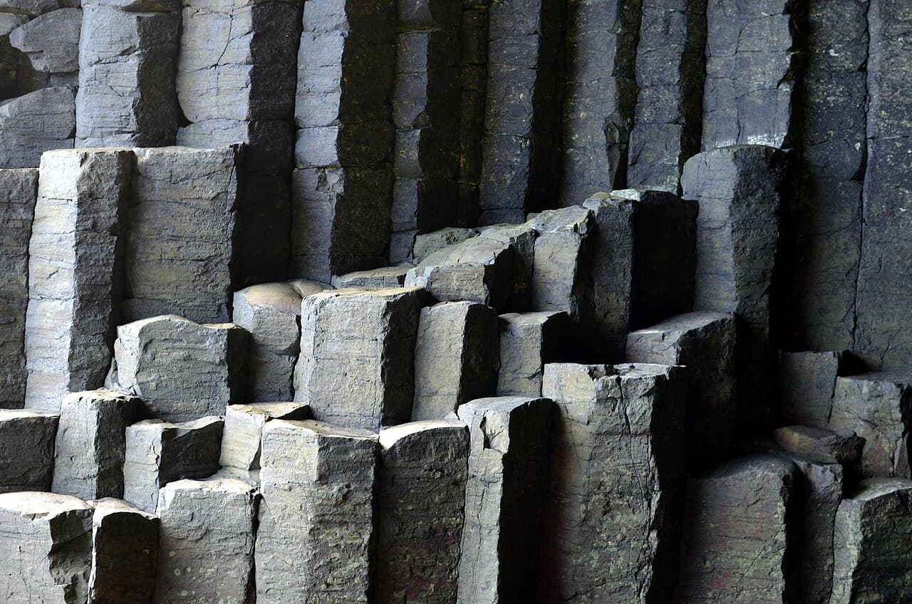 Tiers of fractured hexagonal basalt columns inside Fingal's Cave, their grey faces modelled by soft side light.
